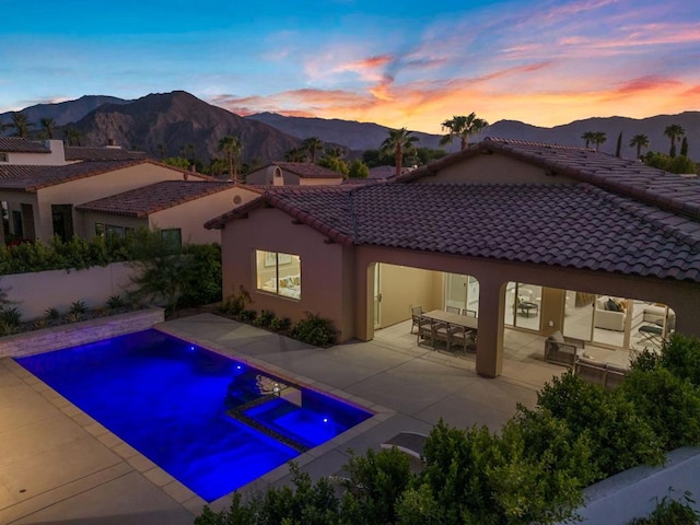 pool at dusk featuring a mountain view, a patio area, and an in ground hot tub