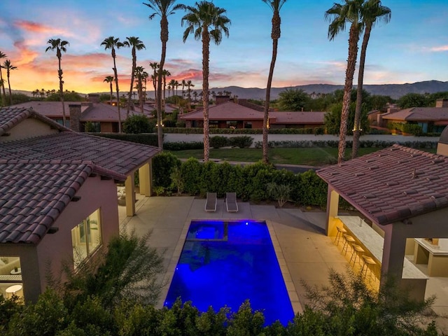 pool at dusk with a patio area and a mountain view