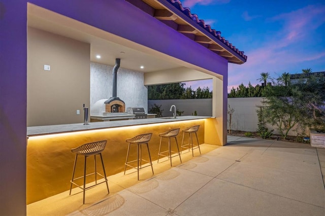 patio terrace at dusk featuring grilling area and a wet bar