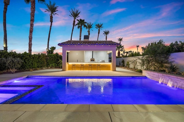 pool at dusk featuring exterior kitchen, a patio area, and a bar