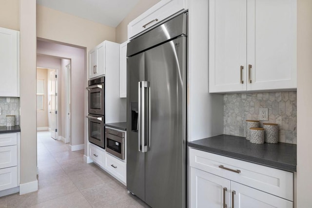 kitchen featuring backsplash, white cabinets, light tile patterned flooring, and appliances with stainless steel finishes