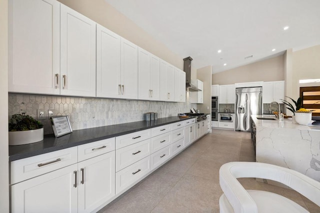 kitchen featuring lofted ceiling, white cabinets, wall chimney range hood, appliances with stainless steel finishes, and tasteful backsplash