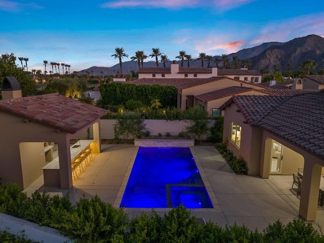 pool at dusk with a mountain view, a patio, and exterior bar