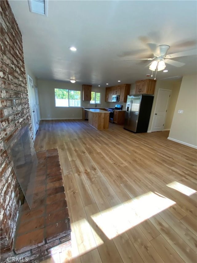 kitchen with a brick fireplace, ceiling fan, light wood-type flooring, and appliances with stainless steel finishes