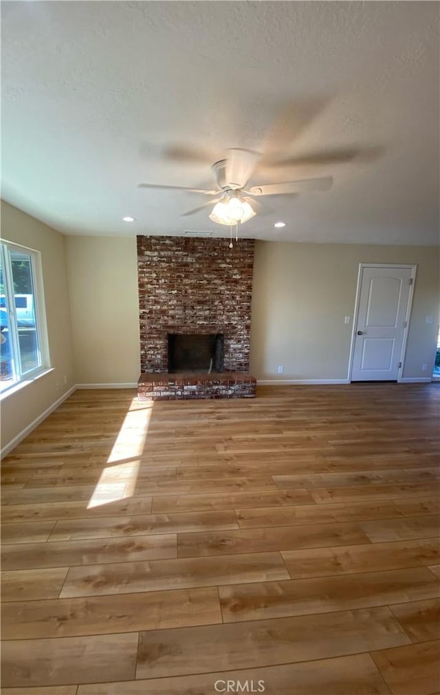 unfurnished living room featuring ceiling fan, light wood-type flooring, a textured ceiling, and a brick fireplace