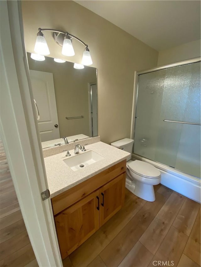 full bathroom with shower / bath combination with glass door, wood-type flooring, vanity, and toilet