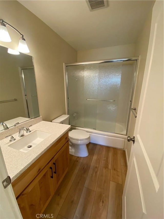 full bathroom featuring hardwood / wood-style floors, vanity, toilet, and enclosed tub / shower combo