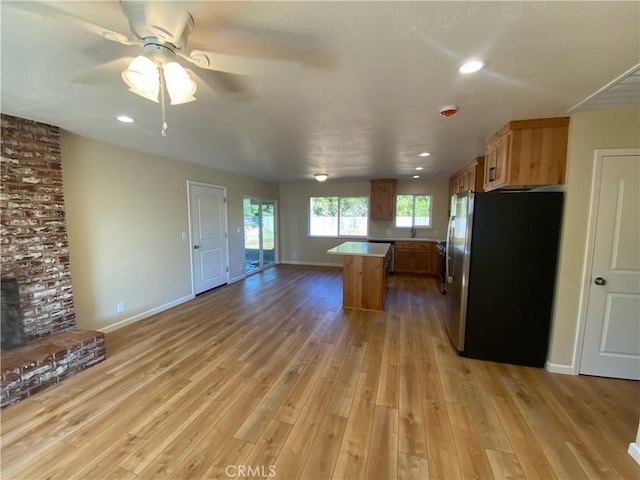 kitchen with a brick fireplace, a kitchen island, ceiling fan, light hardwood / wood-style flooring, and stainless steel refrigerator