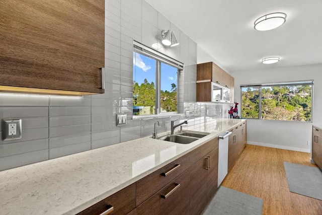 kitchen with light stone countertops, dishwasher, light hardwood / wood-style floors, sink, and backsplash