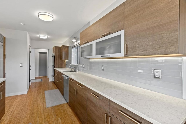 kitchen featuring stainless steel dishwasher, sink, decorative backsplash, and light wood-type flooring