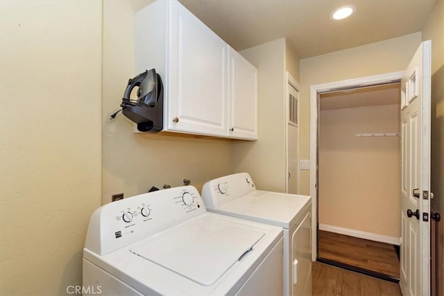 clothes washing area with washer and dryer, cabinets, and hardwood / wood-style flooring