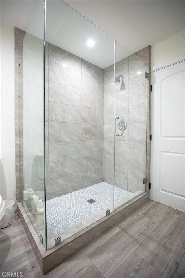 bathroom featuring hardwood / wood-style floors, a shower with shower door, and toilet