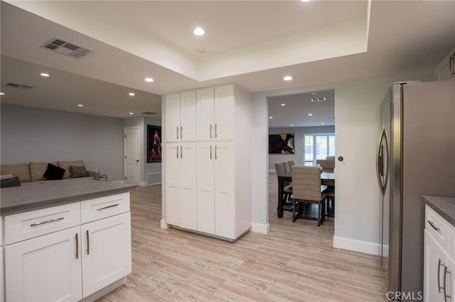 kitchen with a raised ceiling, white cabinetry, stainless steel refrigerator, and light hardwood / wood-style flooring