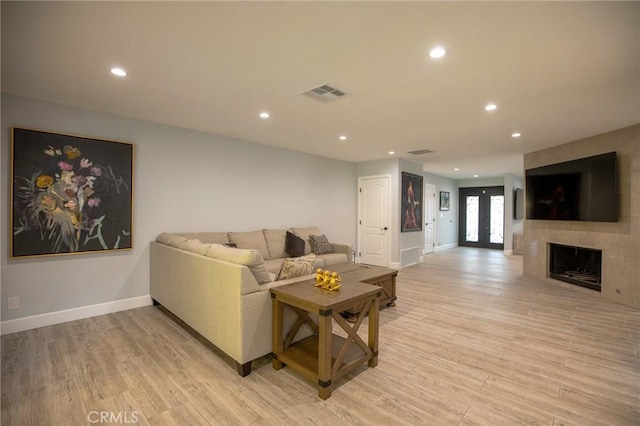 living room featuring a tile fireplace, french doors, and light hardwood / wood-style flooring