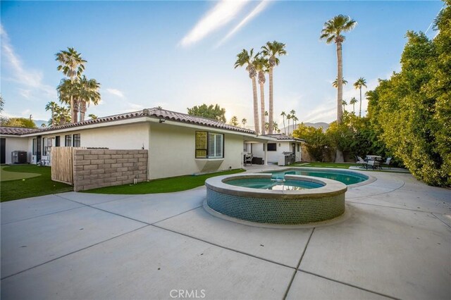 back of property with central AC unit, an in ground hot tub, and a patio