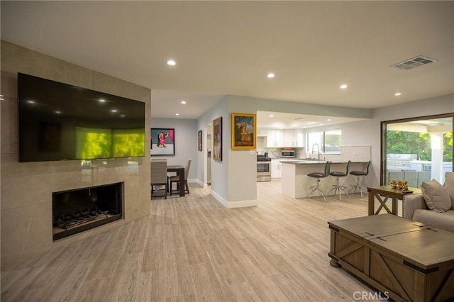 living room with a tiled fireplace, sink, and light wood-type flooring