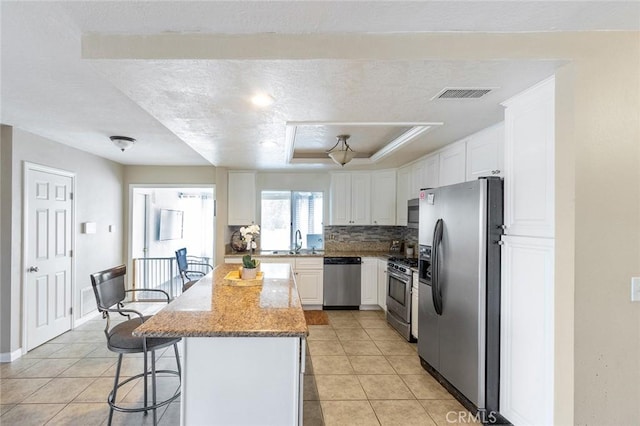 kitchen featuring sink, stainless steel appliances, a kitchen island, light stone counters, and white cabinets