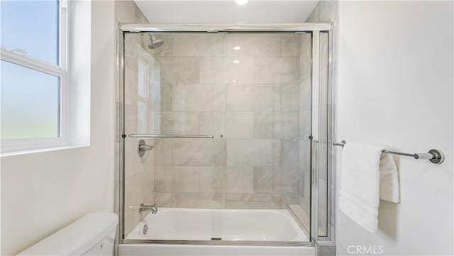 bathroom featuring toilet and shower / bath combination with glass door