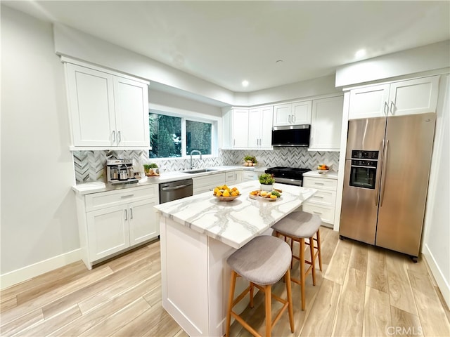 kitchen featuring a breakfast bar, light hardwood / wood-style flooring, appliances with stainless steel finishes, a kitchen island, and white cabinetry