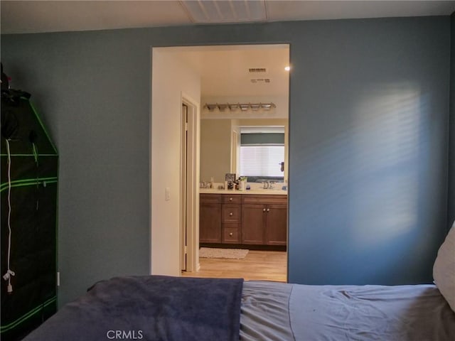 bedroom with ensuite bathroom, sink, and light hardwood / wood-style floors