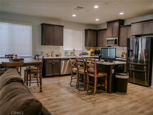 kitchen featuring appliances with stainless steel finishes, a center island, light hardwood / wood-style floors, and dark brown cabinets