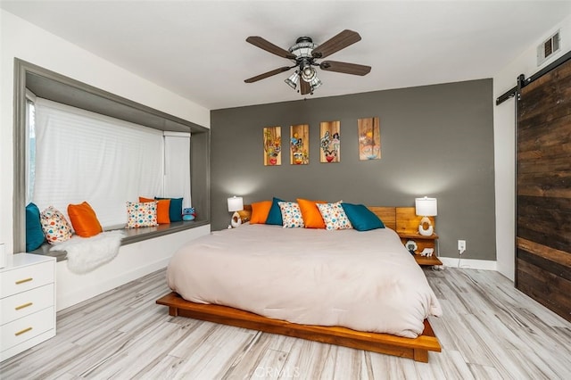 bedroom with a barn door, ceiling fan, and light hardwood / wood-style floors