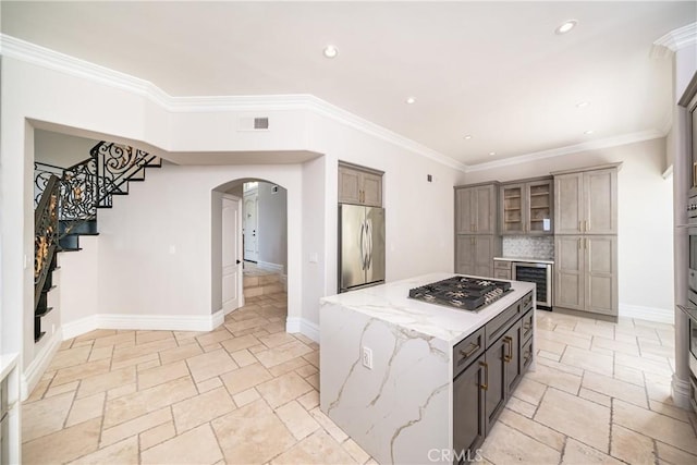 kitchen featuring light stone countertops, stainless steel appliances, wine cooler, crown molding, and a kitchen island