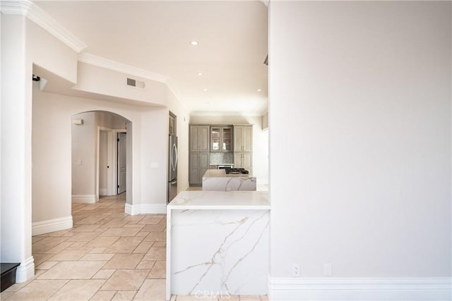 kitchen featuring backsplash, stainless steel refrigerator, light stone counters, and ornamental molding