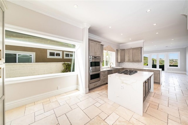 kitchen with a center island, backsplash, light stone countertops, ornamental molding, and stainless steel appliances