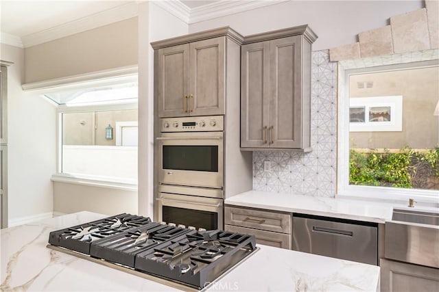 kitchen with stainless steel appliances, light stone counters, a healthy amount of sunlight, and crown molding