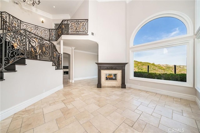 unfurnished living room featuring a tile fireplace, ornamental molding, and a towering ceiling