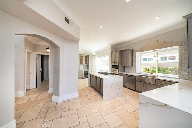 kitchen featuring sink, a center island, stainless steel appliances, tasteful backsplash, and light stone counters