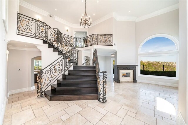 stairway featuring a fireplace, a high ceiling, ornamental molding, and a notable chandelier