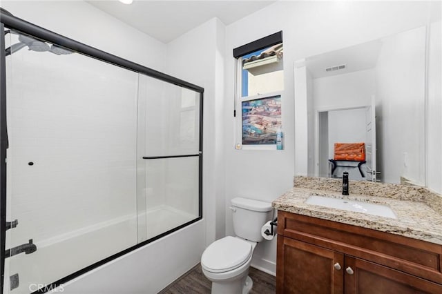 full bathroom featuring shower / bath combination with glass door, hardwood / wood-style floors, vanity, and toilet