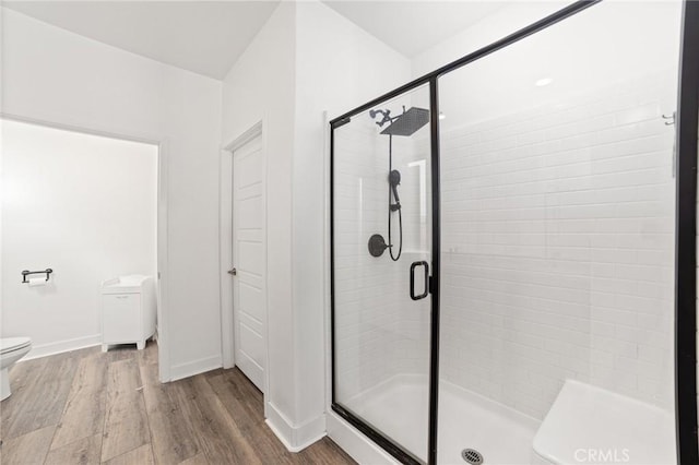 bathroom with hardwood / wood-style floors, toilet, and a shower with door