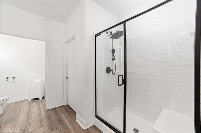 bathroom with wood finished floors, a shower stall, toilet, and baseboards