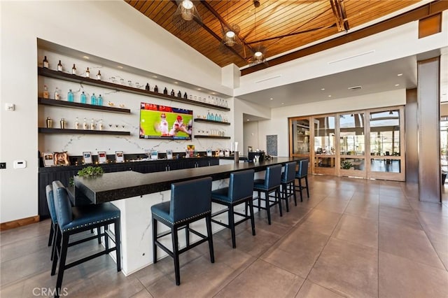 bar with high vaulted ceiling, wooden ceiling, baseboards, tile patterned floors, and wet bar