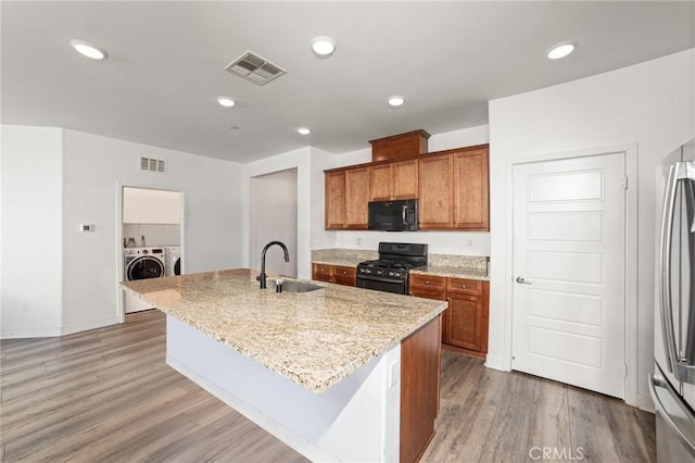 kitchen featuring visible vents, an island with sink, washer and dryer, black appliances, and a sink