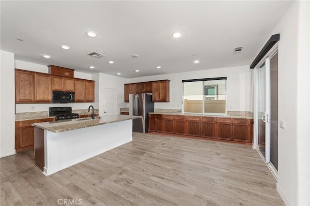 kitchen featuring visible vents, a sink, light wood-style flooring, and black appliances