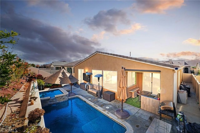 pool at dusk with an in ground hot tub, a patio area, and a grill