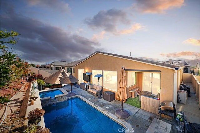 pool at dusk with area for grilling, a patio area, a fenced backyard, and a pool with connected hot tub