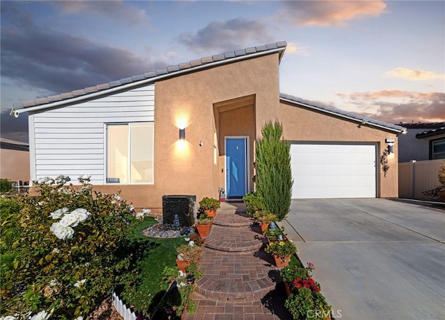 view of front of property with concrete driveway, an attached garage, fence, and stucco siding