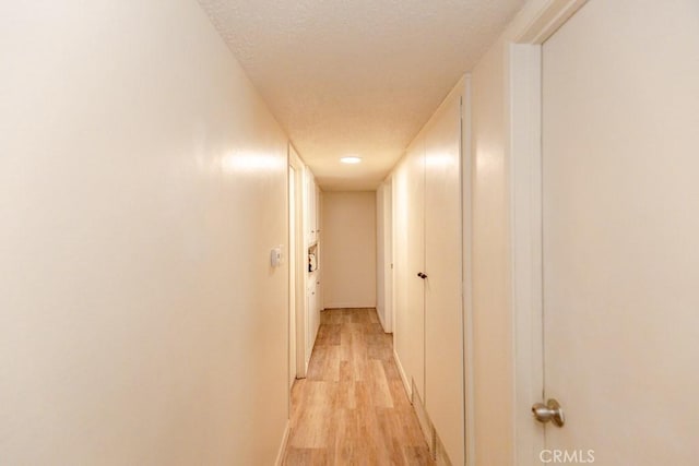 corridor with a textured ceiling and light hardwood / wood-style floors