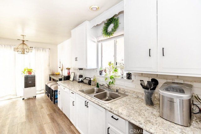 kitchen with sink, hanging light fixtures, a notable chandelier, light hardwood / wood-style floors, and white cabinets