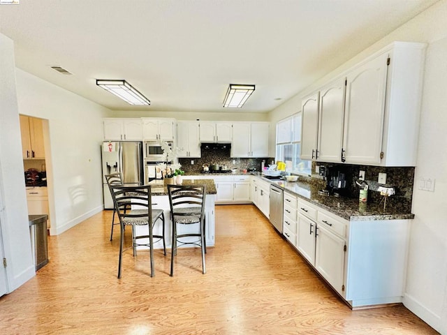 kitchen with a kitchen island, dark stone countertops, appliances with stainless steel finishes, light hardwood / wood-style floors, and white cabinetry