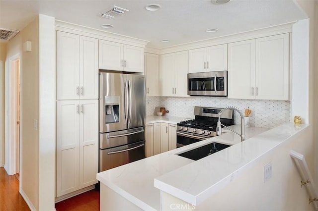 kitchen with backsplash, kitchen peninsula, hardwood / wood-style flooring, appliances with stainless steel finishes, and white cabinets