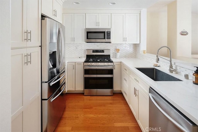 kitchen with white cabinetry, stainless steel appliances, backsplash, light stone countertops, and sink