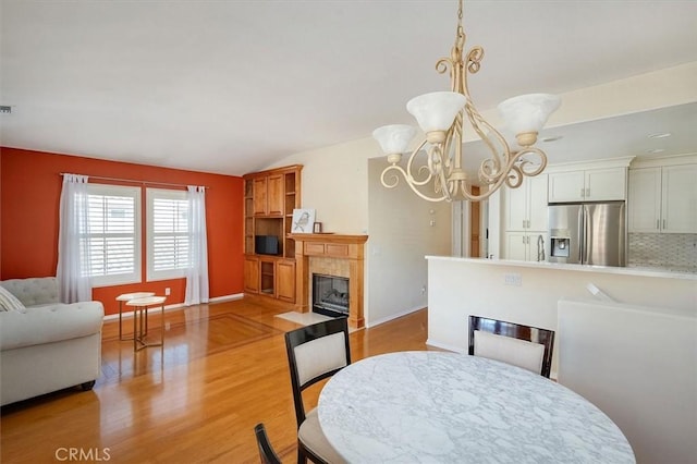 dining room featuring vaulted ceiling, sink, an inviting chandelier, light wood-type flooring, and a tiled fireplace