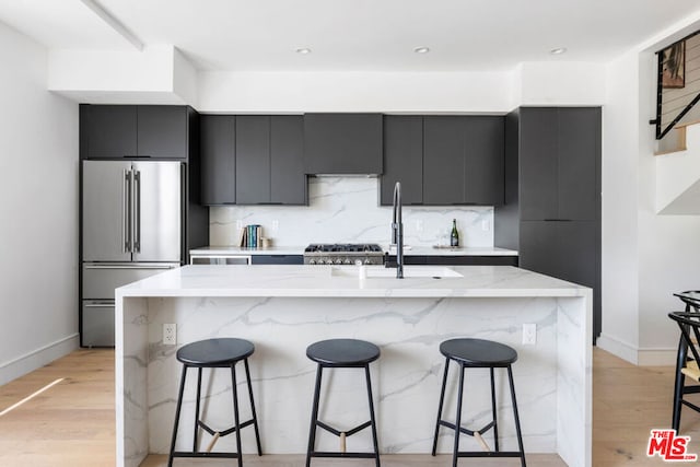 kitchen featuring a kitchen bar, a center island with sink, stainless steel appliances, and light hardwood / wood-style flooring