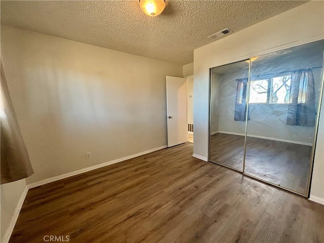 unfurnished bedroom with a textured ceiling, dark hardwood / wood-style floors, and a closet